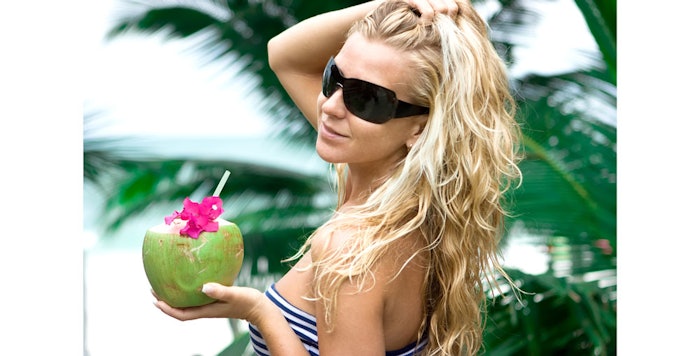 Woman in sunglasses holds coconut in hand.