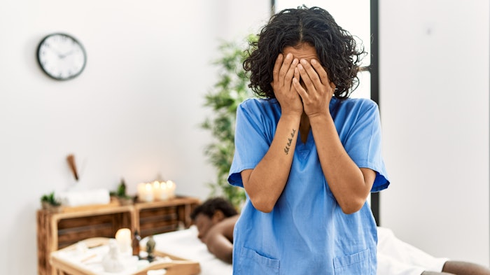 Young therapist woman at wellness spa center with sad expression covering face with hands while crying