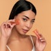 A young Asian woman with clean radiant skin makes a vacuum massage of the face with silicone facial cups on a beige background. Spa care, cupping.