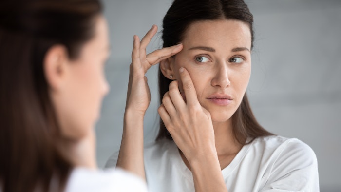Anxious young woman look in the mirror worried about wrinkle or acne on unhealthy skin