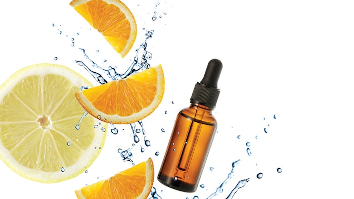 Dark brown glass bottle of face serum with vitamin C or essential oil and orange slices flying in splashing water