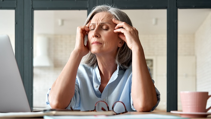 Tired stressed old mature business woman suffering from headache at work. Upset sick senior middle aged lady massaging head feeling migraine from overwork or menopause using computer at home