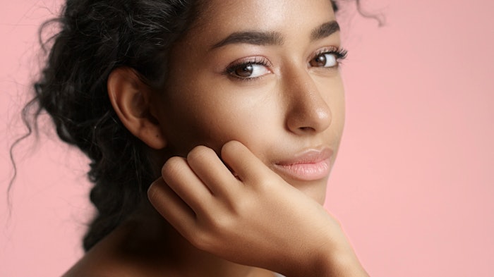 Close up of a happy and relaxed young woman with perfect olive skin fixing her wavy black hair isolated on white