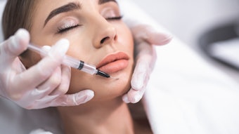 Beauty procedure. Close up portrait of attractive young lady with closed eyes and beautician arms with syringe