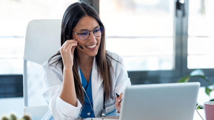 Female doctor talking with colleagues through a video call with a laptop in the consultation.