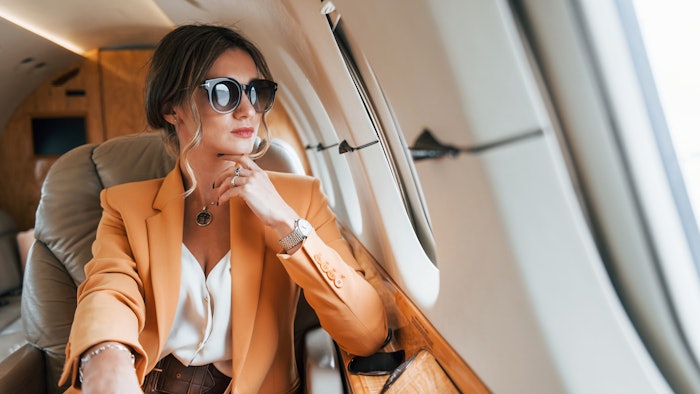 In sunglasses. Young passenger woman in yellow clothes is flying in the plane