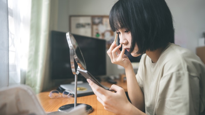 Young adult asian woman makeup and face skin care using mobile phone for streaming content creator at home.