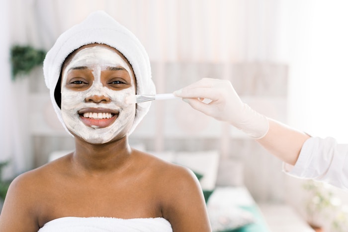 Young African woman in Studio doing body care with refreshing facial mask for young and beautiful skin and relaxation