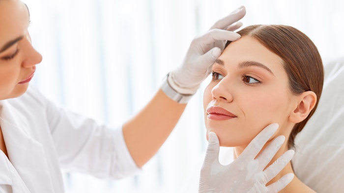 Cosmetologist in gloves checking face of woman