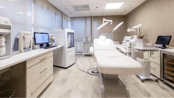Advanced biorevitalization devices, including lasers and microneedling pens, organized in a sleek, modern treatment room. the clean, professional setting features state-of-the-art equipment, white chairs, and sophisticated artwork.