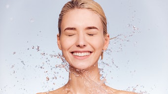 Photo of young woman with clean skin and splash of water. Portrait of smiling woman with drops of water around her face.