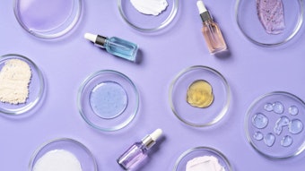 Cosmetic products, scrub, face serum and gel in many petri dishes on a violet background. Cosmetics laboratory research concept.