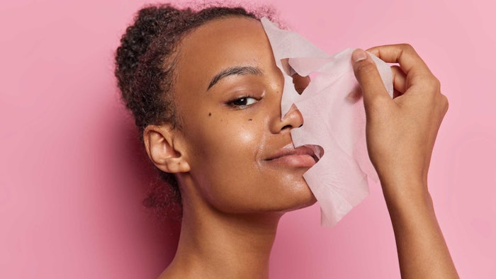 beautiful black woman peeling off facial mask smiling pink background