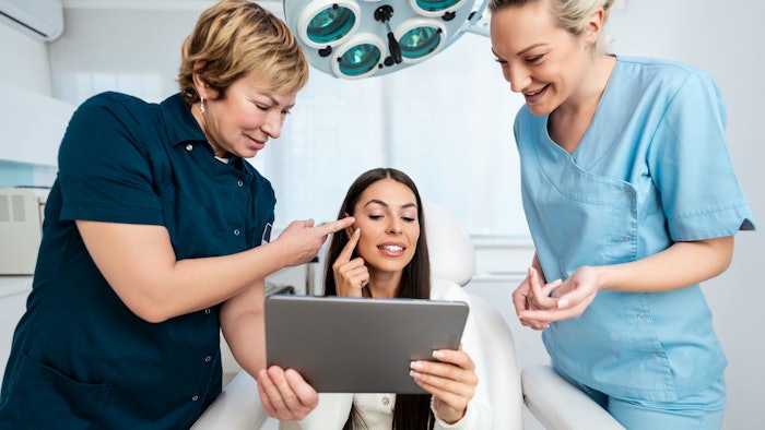 Beautiful and happy brunette woman at beauty medical clinic. She is sitting and talking with two female doctors about face aesthetic treatment.