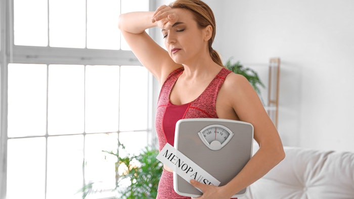 Sporty mature woman holding paper with word MENOPAUSE and weight scales at home