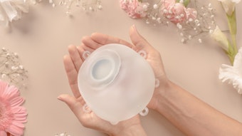 Motive breast implant being held in woman's cupped hands against peach background.