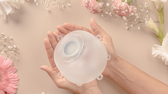 Motive breast implant being held in woman's cupped hands against peach background.