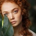 beautiful redhead holding jungle foliage near face