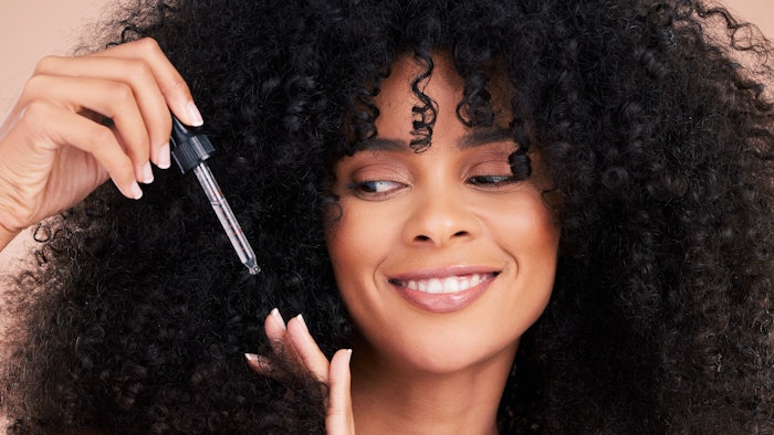 black woman curly hair using serum smiling
