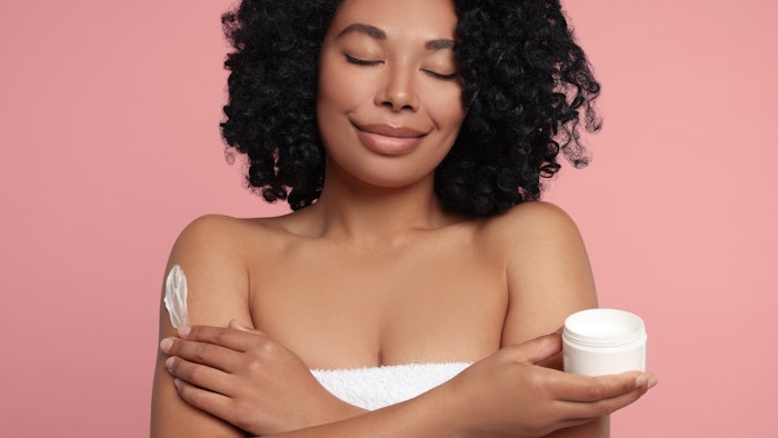 ethnic woman relaxed soothed using body cream pink background