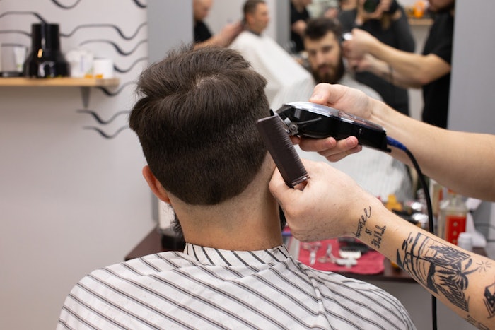 Client receiving a haircut from a barber in a barbershop/salon.