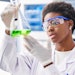 beautiful black female chemist examining liquid in flask