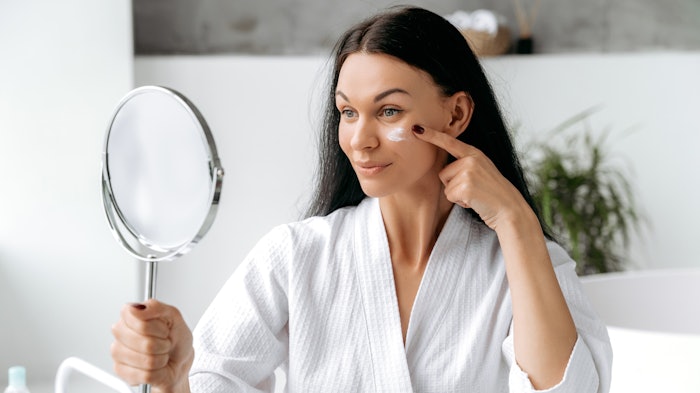 Woman In White Robe Applying Lotion In Bathroom Plant In Background