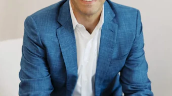 Professional headshot of a smiling man in a blue blazer and white shirt against a neutral background