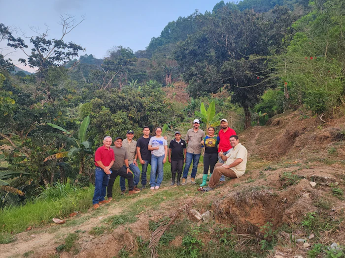 Group of people standing together on cleared land with forested mountains in the background