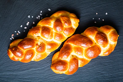 Three golden braided challah loaves arranged on dark slate with sea salt crystals