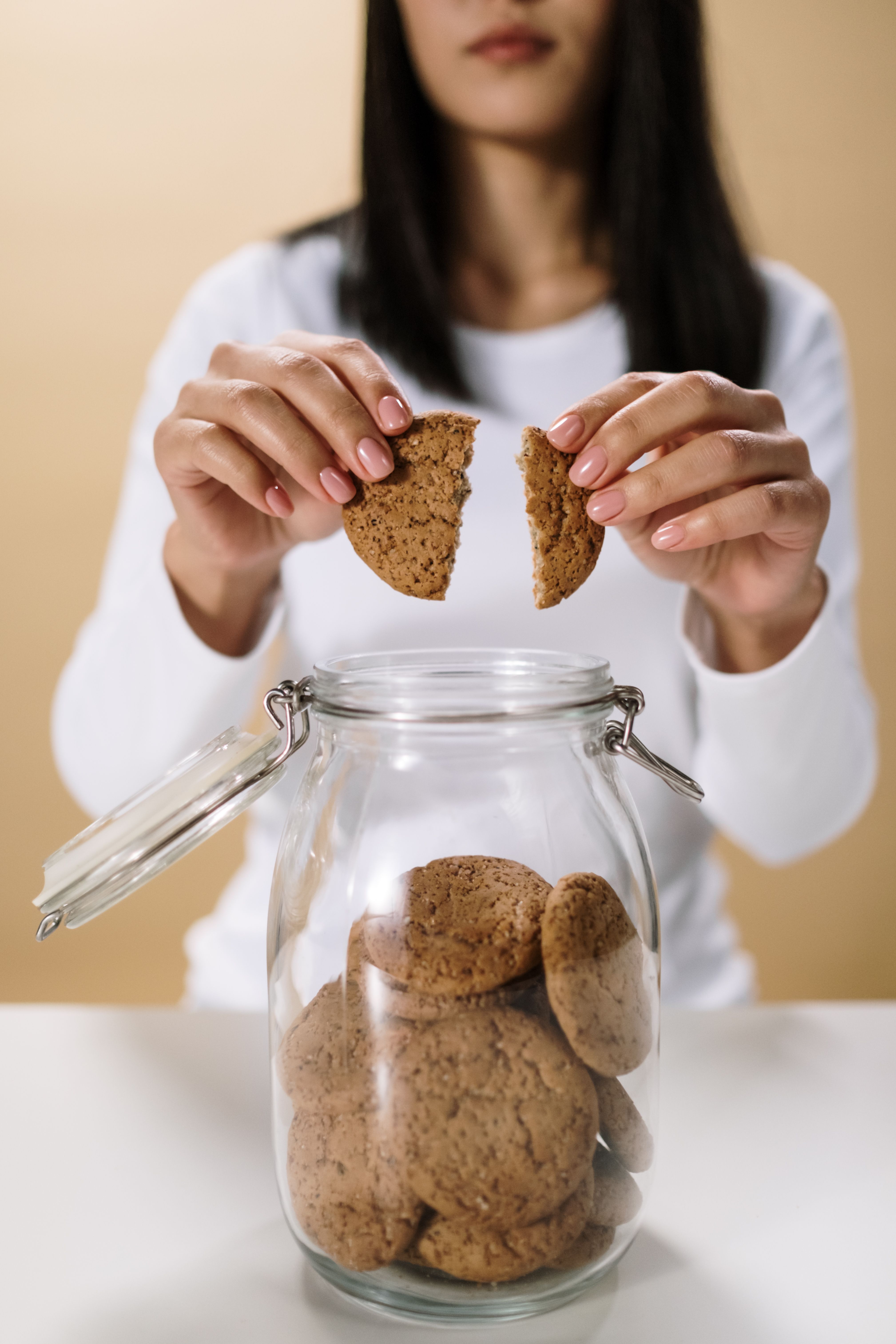 Woman breaking a cookie in half above a glass jar filled with homemade cookies