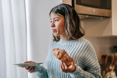 Woman in light blue sweater holding a pretzel and plate in a modern kitchen