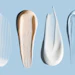 Array of cosmetic and skincare product swatches in white, cream, and pink tones on blue background