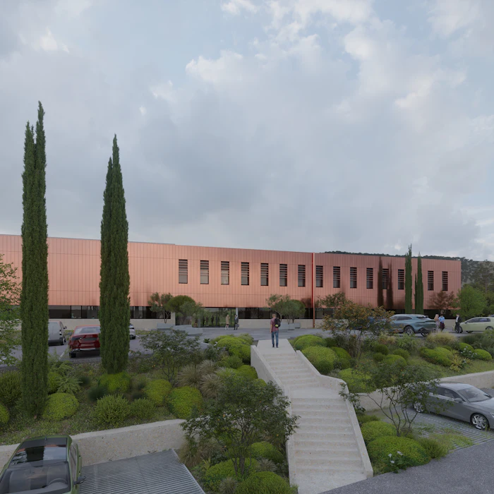 Modern terracotta building with cypress trees, landscaped grounds, and parking area under cloudy sky