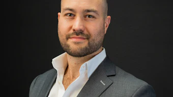 Professional headshot of a man in gray blazer and white shirt against dark background