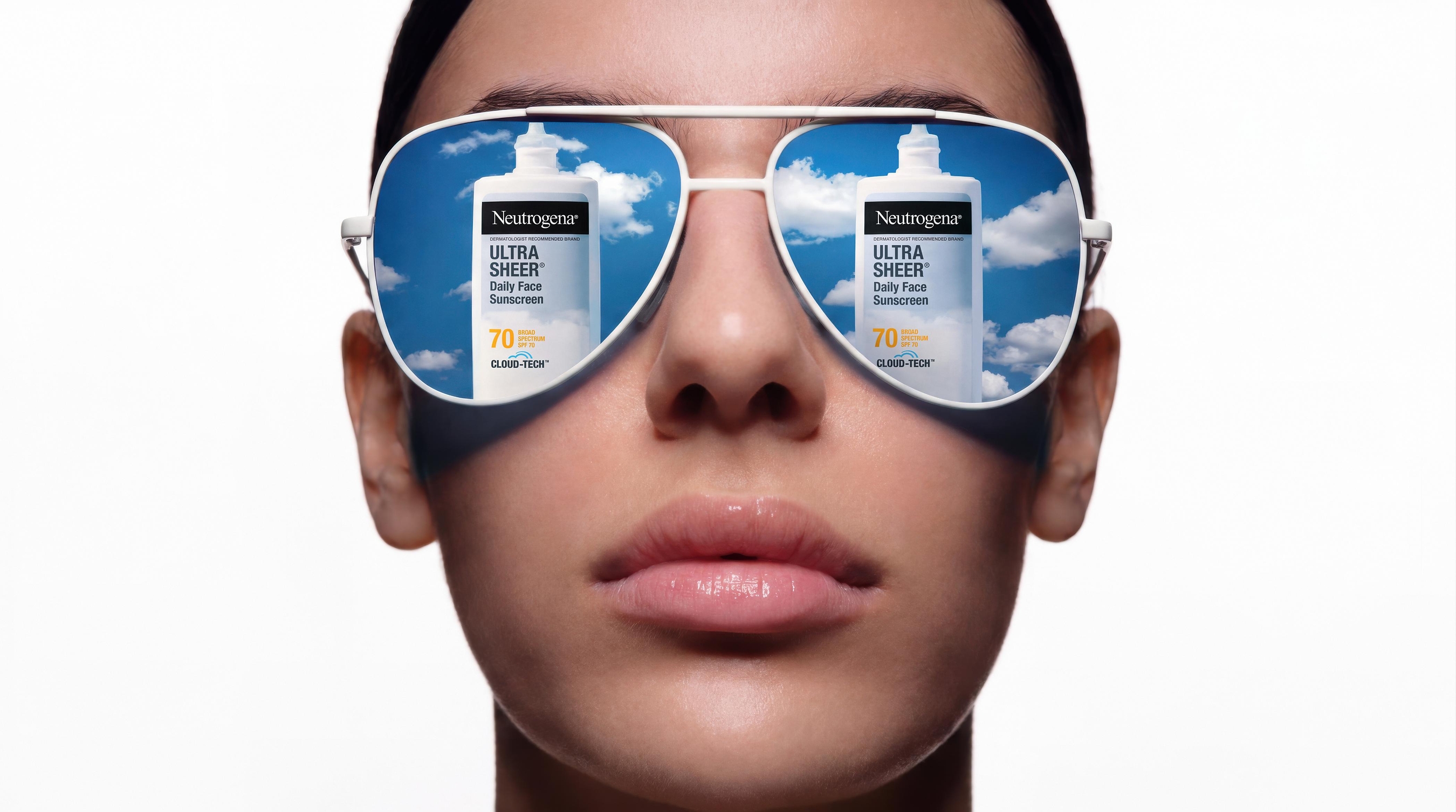 Person wearing oversized aviator sunglasses with Neutrogena Ultra Sheer sunscreen product displayed on blue sky lenses