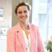 Professional woman smiling in office wearing pink blazer and beaded necklace