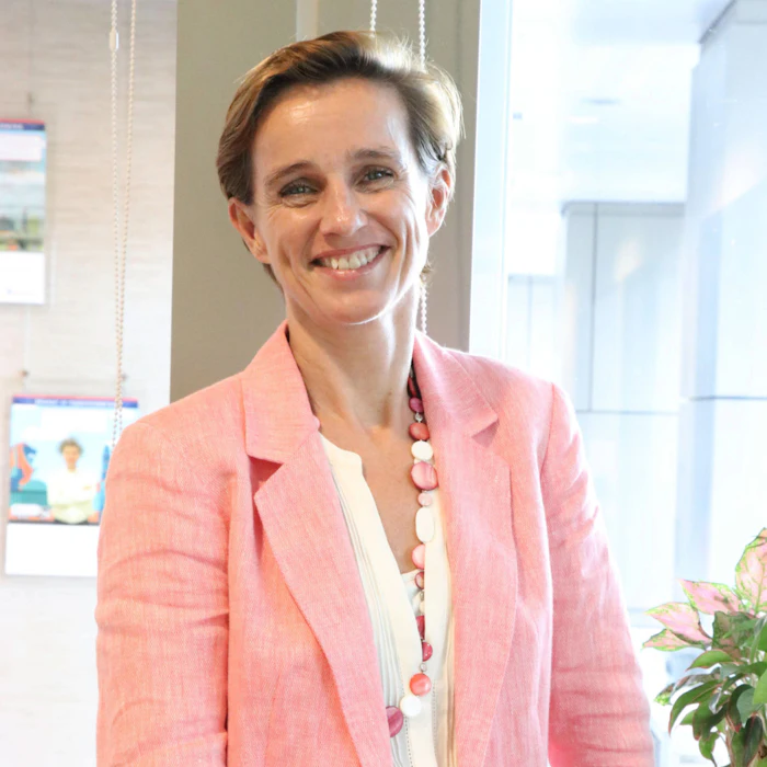 Professional woman smiling in office wearing pink blazer and beaded necklace