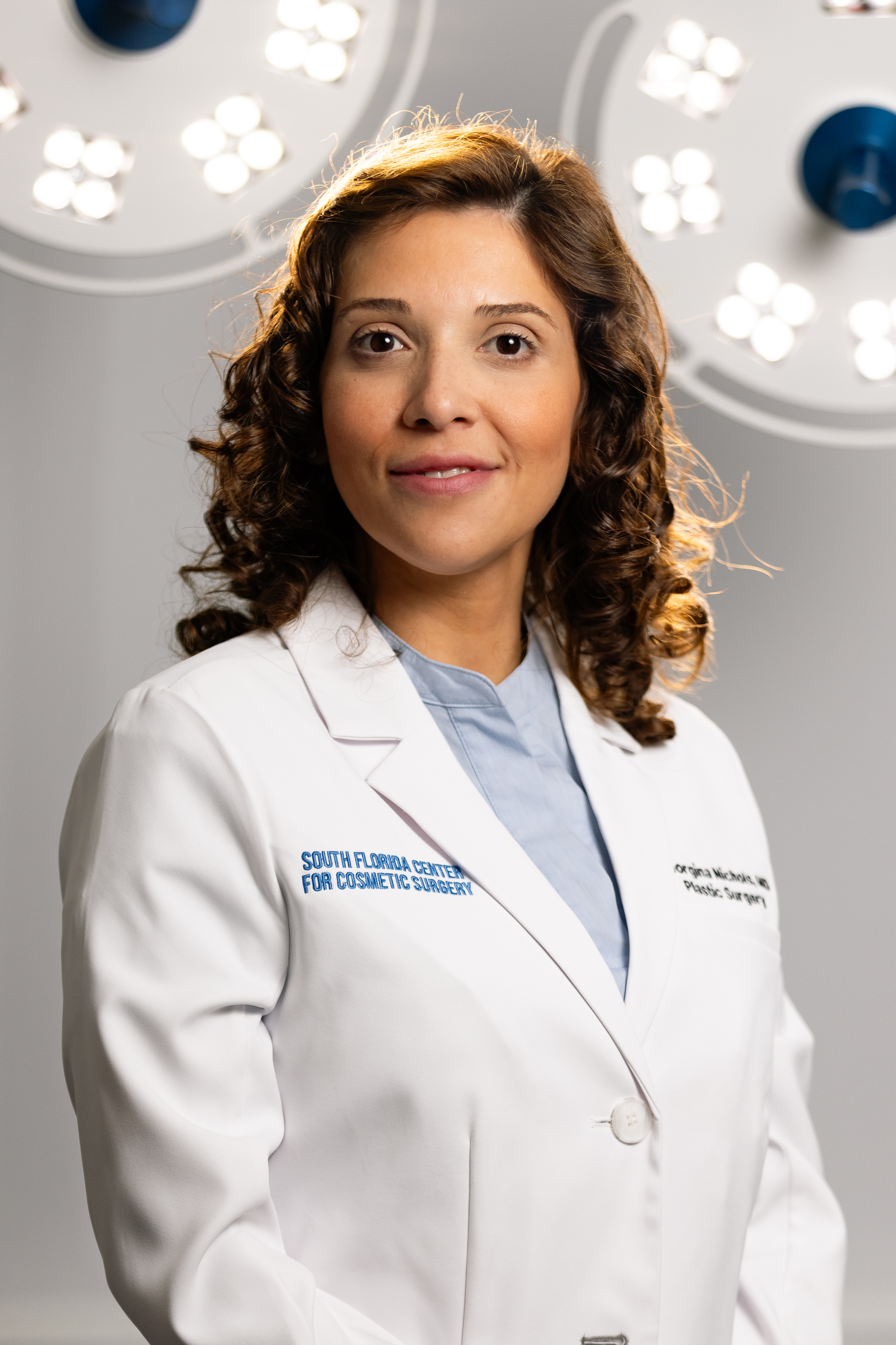 Female cosmetic surgeon in white lab coat at South Florida Center for Cosmetic Surgery, standing in front of surgical lights
