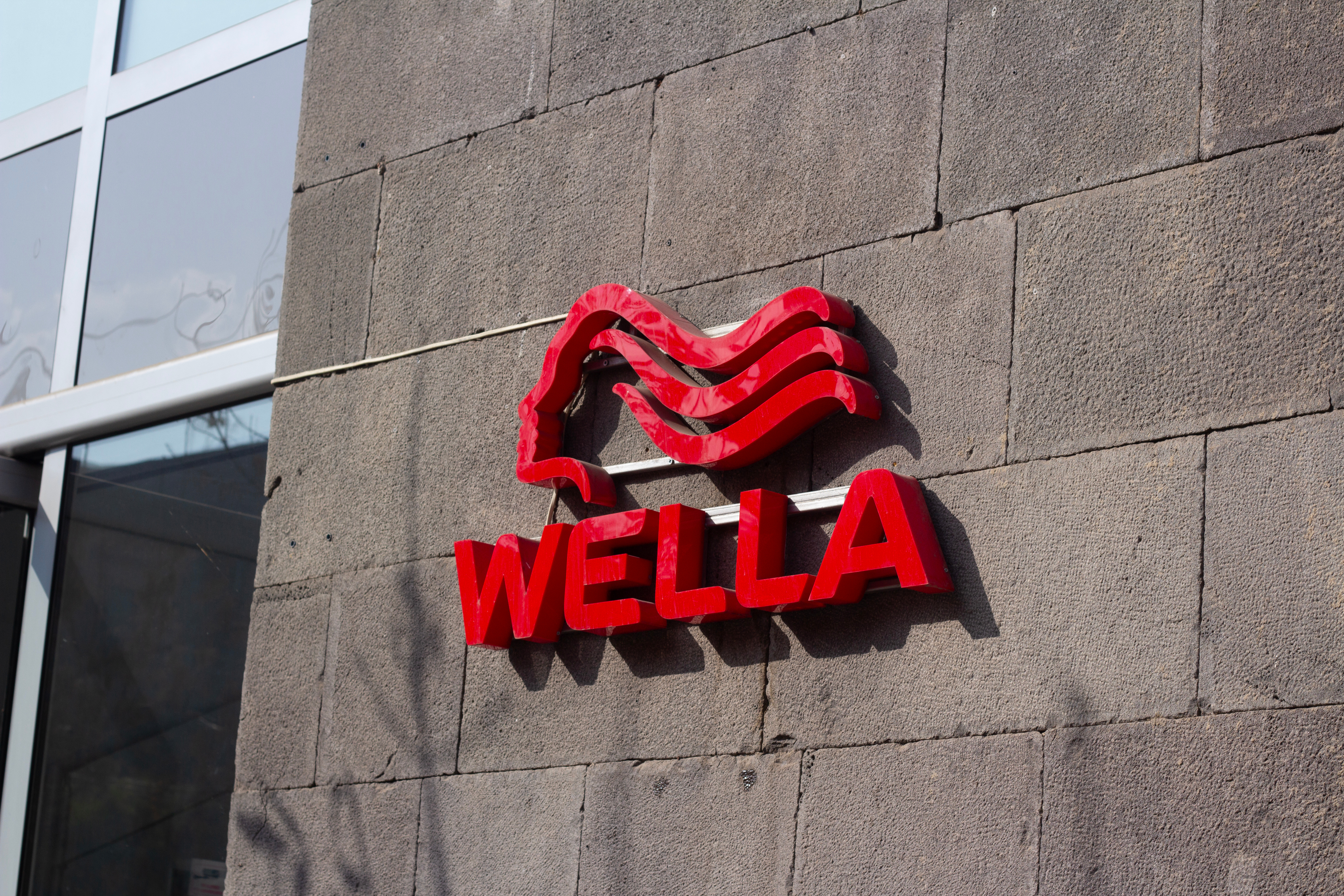 Wella red neon logo sign mounted on concrete building wall