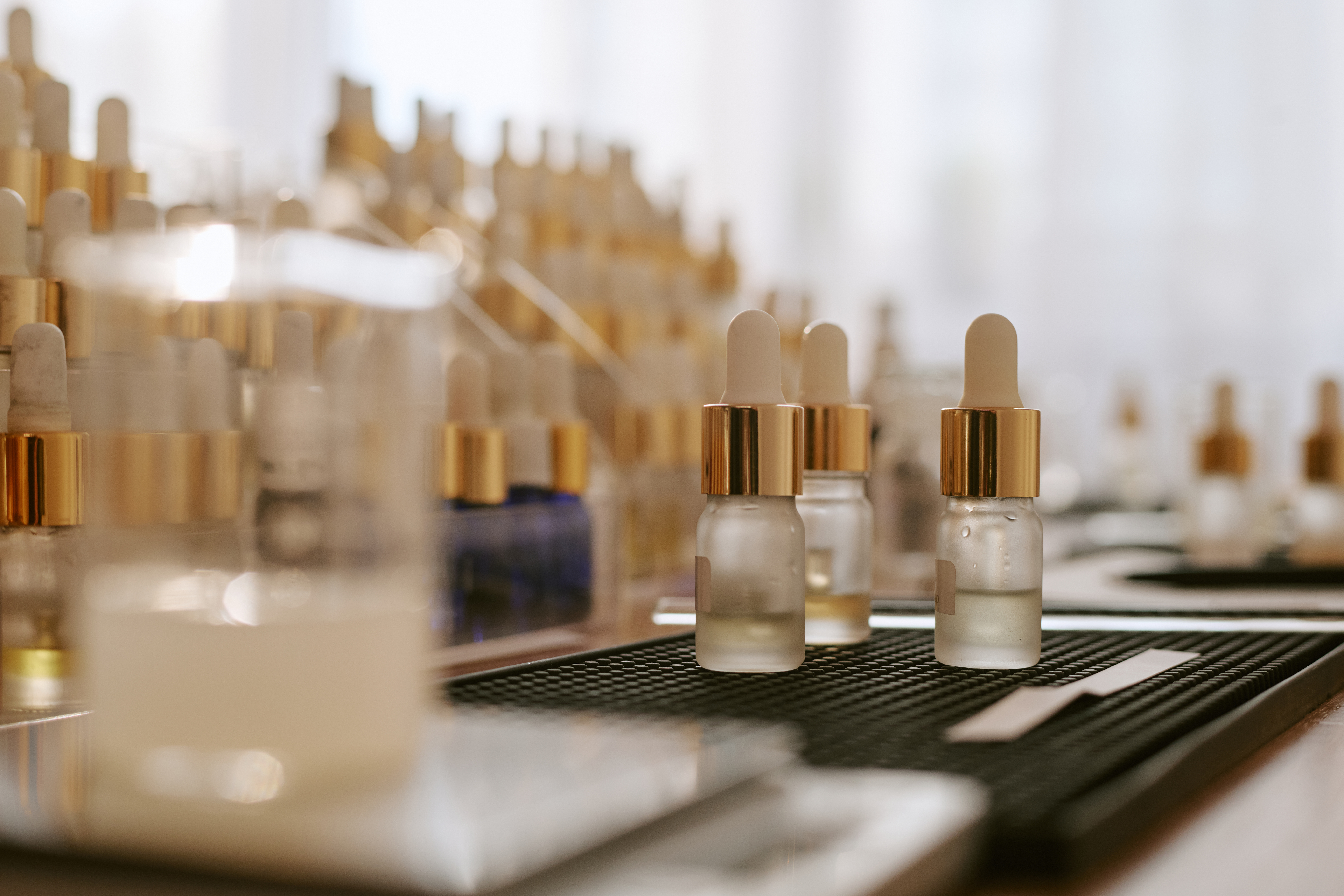 Collection of luxury cosmetic serum bottles with gold dropper caps displayed on black and white surfaces