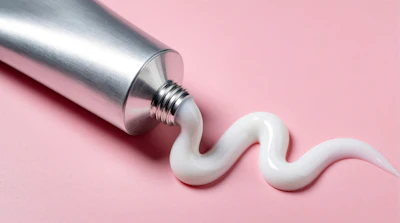 Silver metallic tube dispensing white cream product on pink background