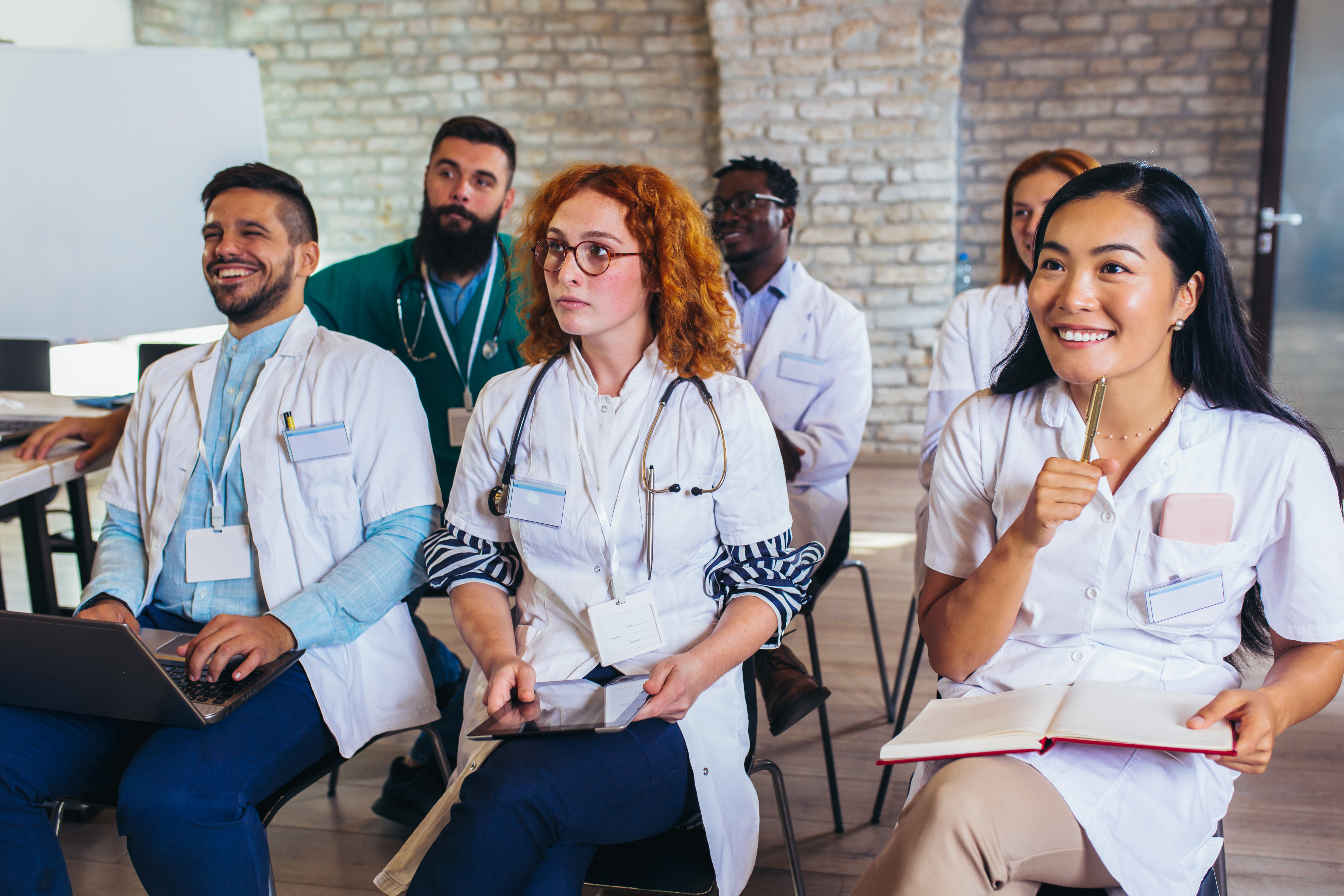 Diverse group of smiling healthcare professionals wearing white coats and ID badges in a modern brick office setting