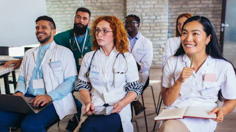 Diverse group of smiling healthcare professionals wearing white coats and ID badges in a modern brick office setting