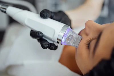 Professional microneedling pen with purple light attachment held during skincare treatment procedure