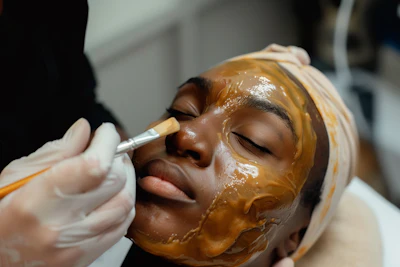 Aesthetician applying golden facial mask to client's face during professional spa treatment