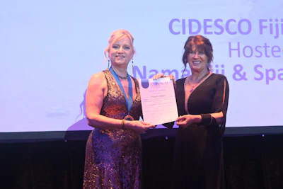 Two women on stage at CIDESCO awards ceremony, one presenting a certificate to the other