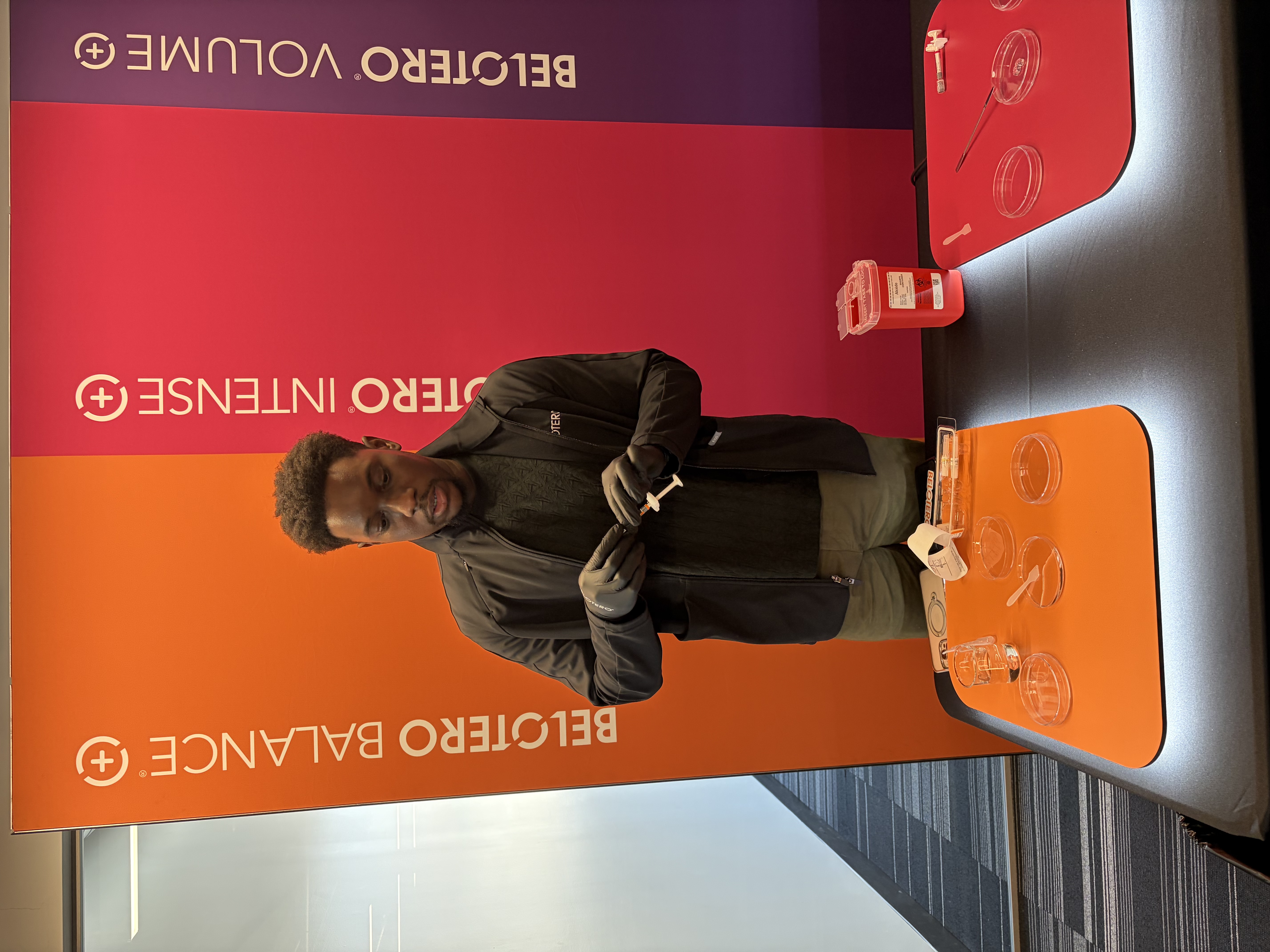 Man in black jacket stands at branded display table with orange and red materials against Beltoro signage backdrop