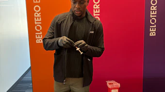 Man in black jacket stands at branded display table with orange and red materials against Beltoro signage backdrop