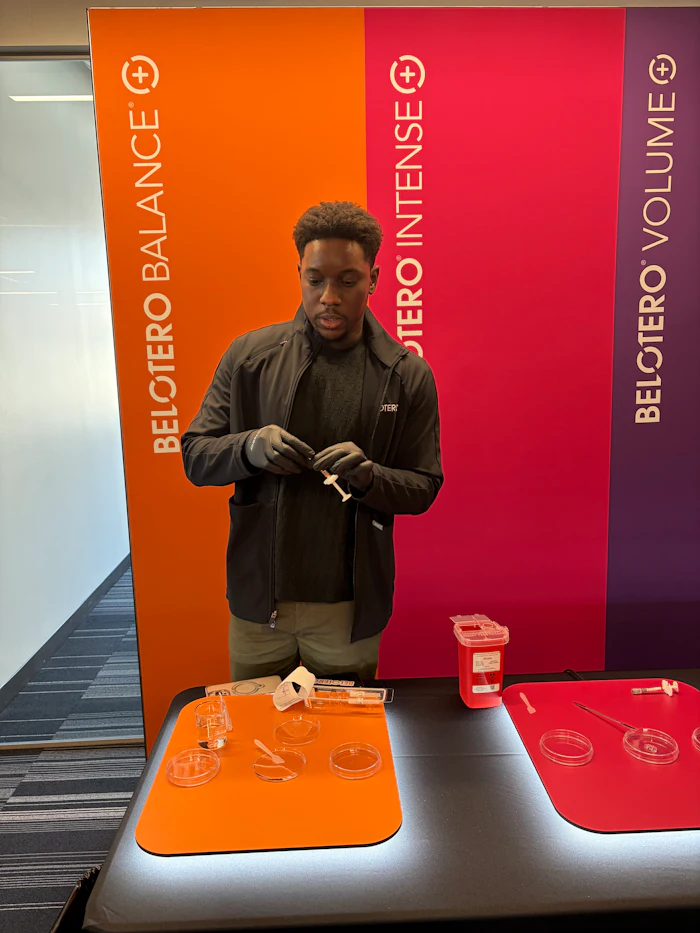 Man in black jacket stands at branded display table with orange and red materials against Beltoro signage backdrop